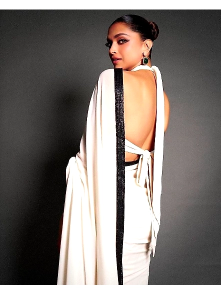 A woman draped in a white sari with a black border, adorned with sequence work and lace, reflecting 