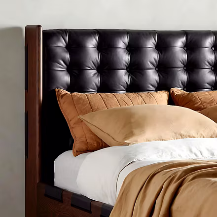 Close-up of handcrafted teak frame and tufted black headboard with beige bedding.
