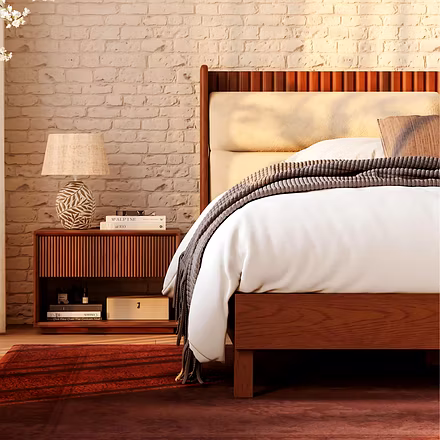 Side angle of king or queen size teakwood bed with cushioned headboard and matching wooden bedside t