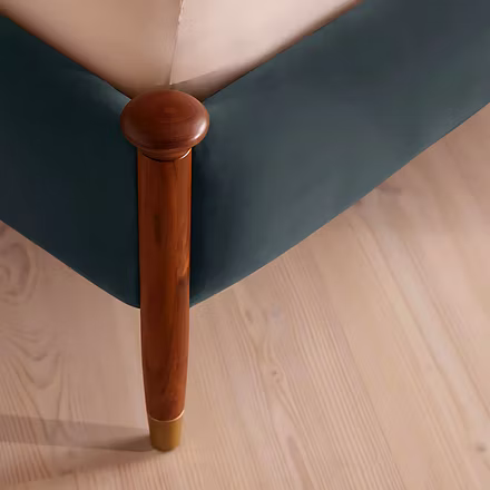 Corner detail of upholstered bed with teakwood pillar and brass accent, king and queen size options.
