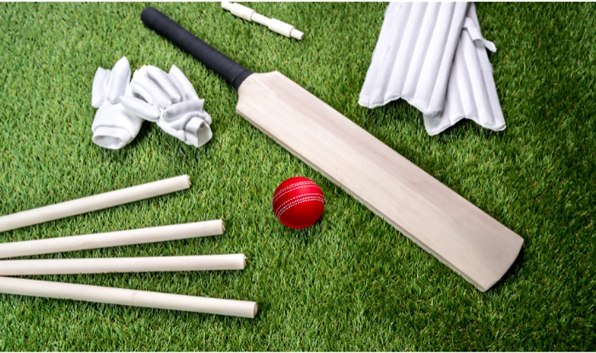 Cricket equipment including helmet, cricket bat, gloves, and pads laid out on the grass, ready for p