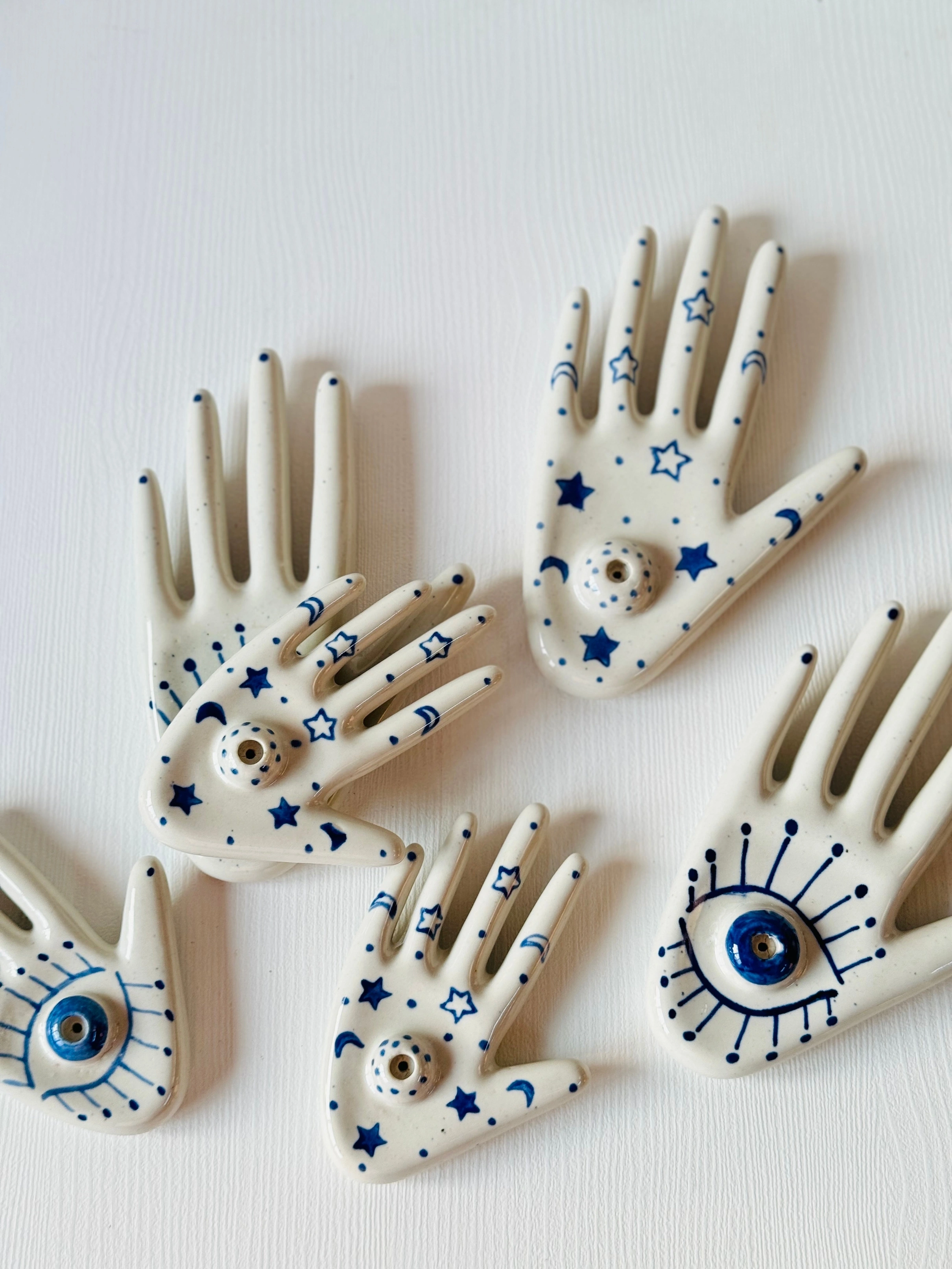 Five ceramic hand-shaped amulets with blue eye and star decorations on a white background.