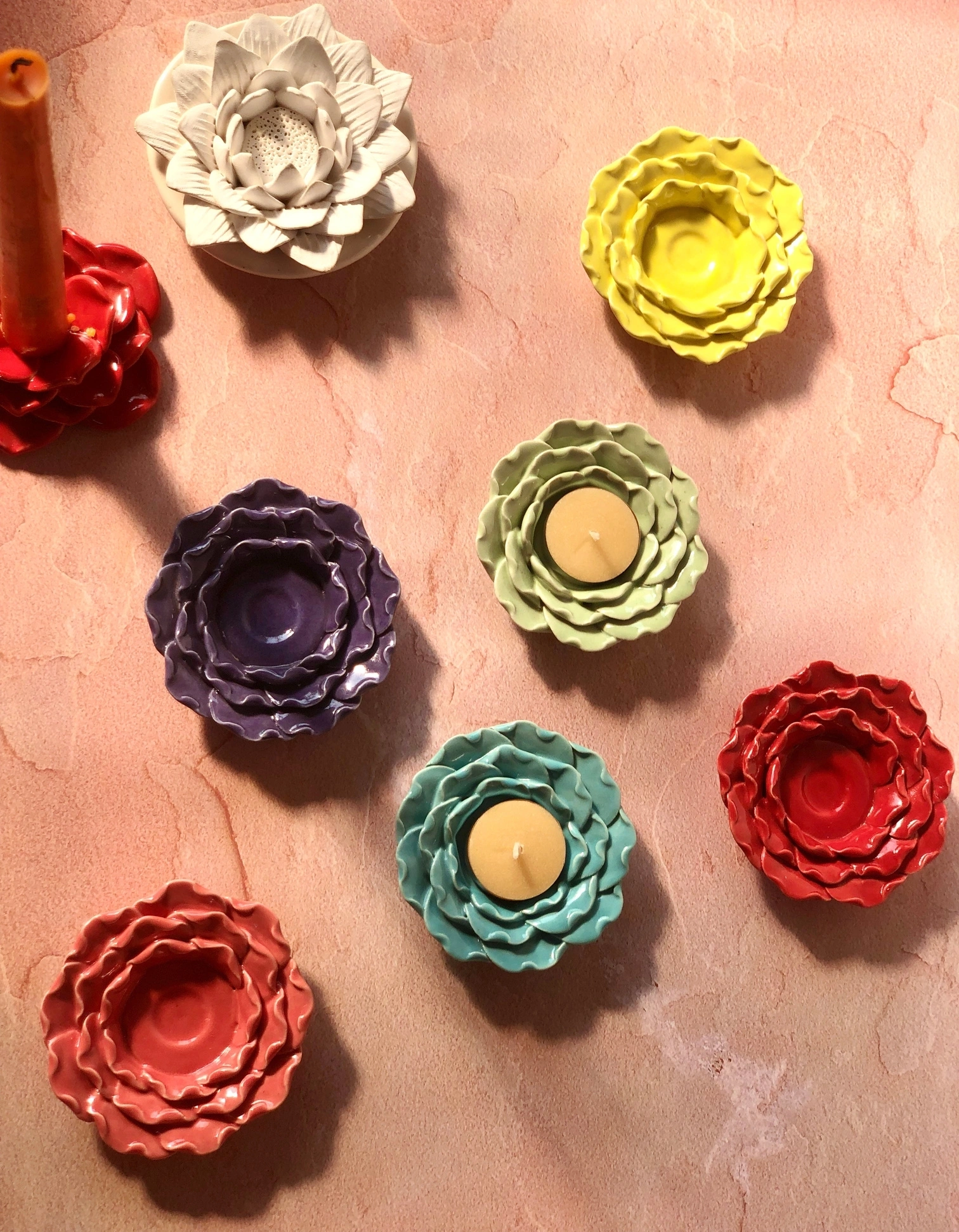 Colorful ceramic flower-shaped candle holders with a lit candle on a textured surface.