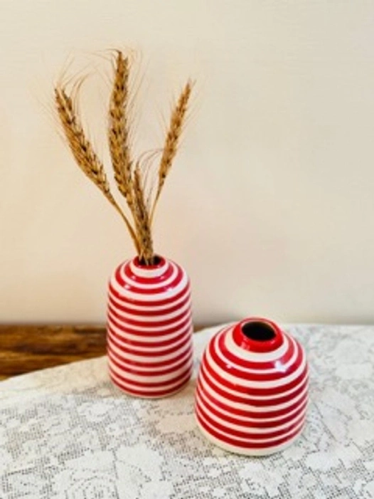 Two striped red and white vases on a table, one with wheat stalks.