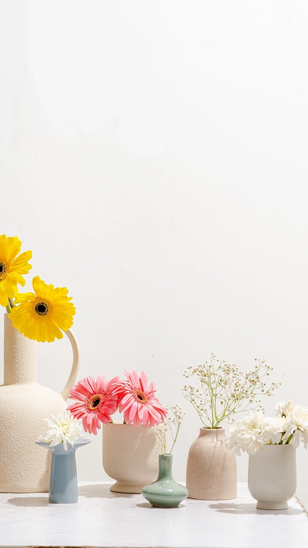 A collection of colorful flowers arranged in various vases on a white background.