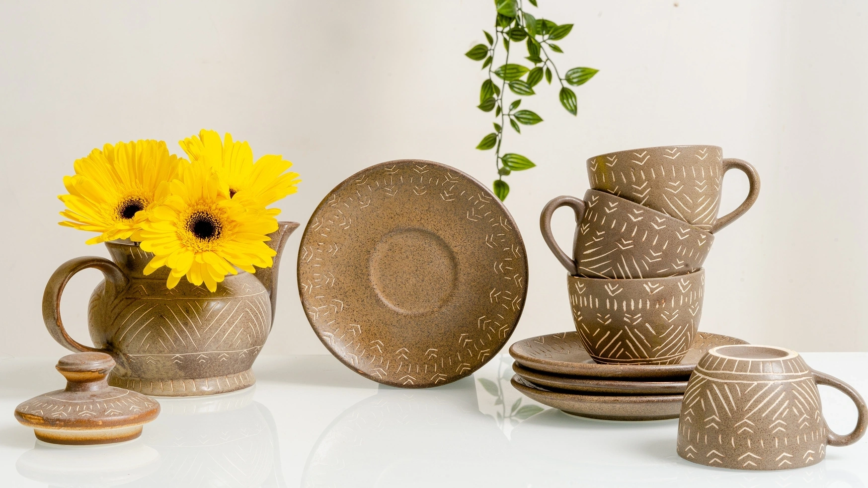 Ceramic pottery and stacked cups with engraved patterns, a jug with yellow daisies, and a green plan