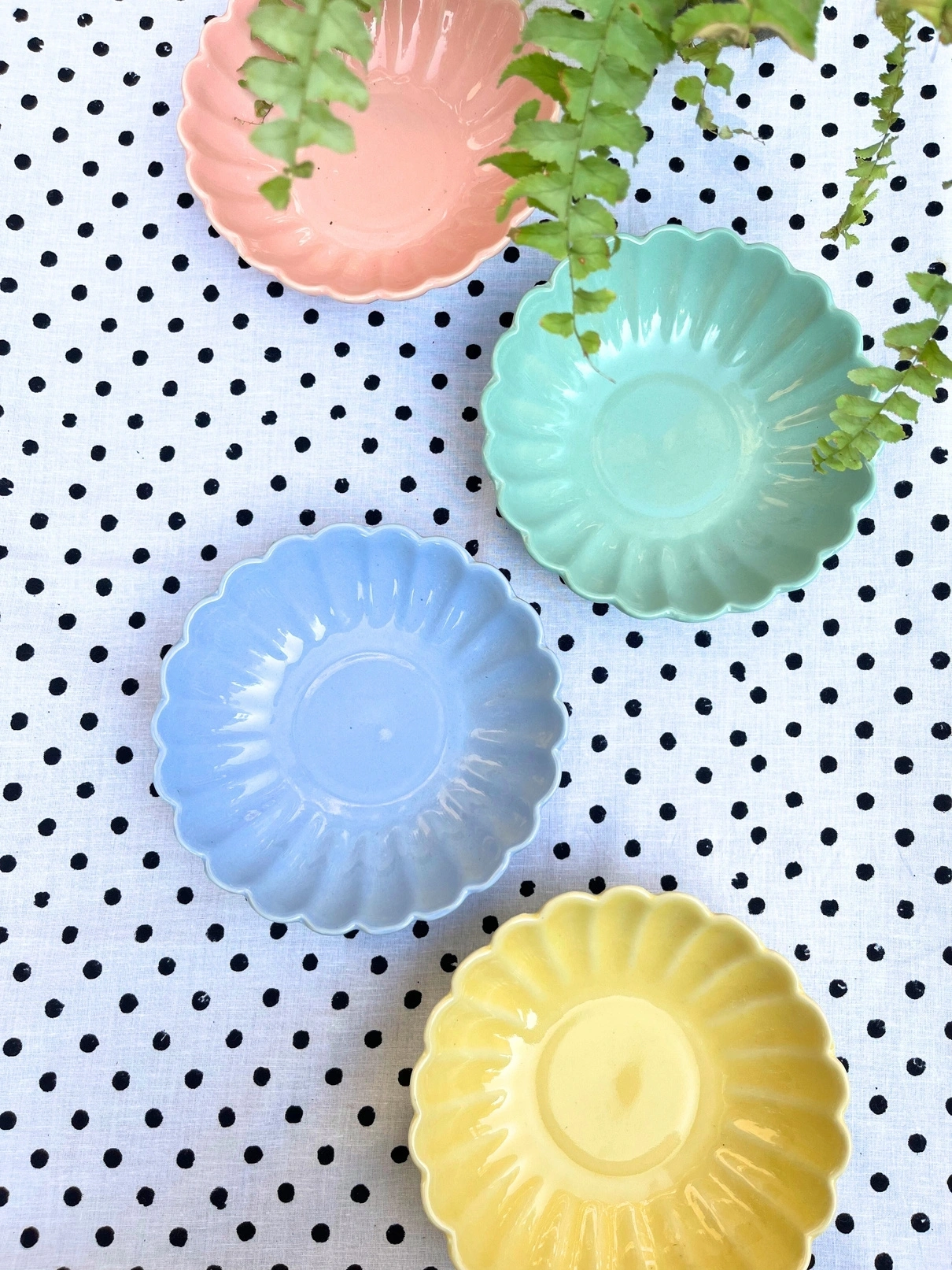 Four colorful ceramic dishes on a polka-dotted tablecloth, with a small plant overhanging one dish.