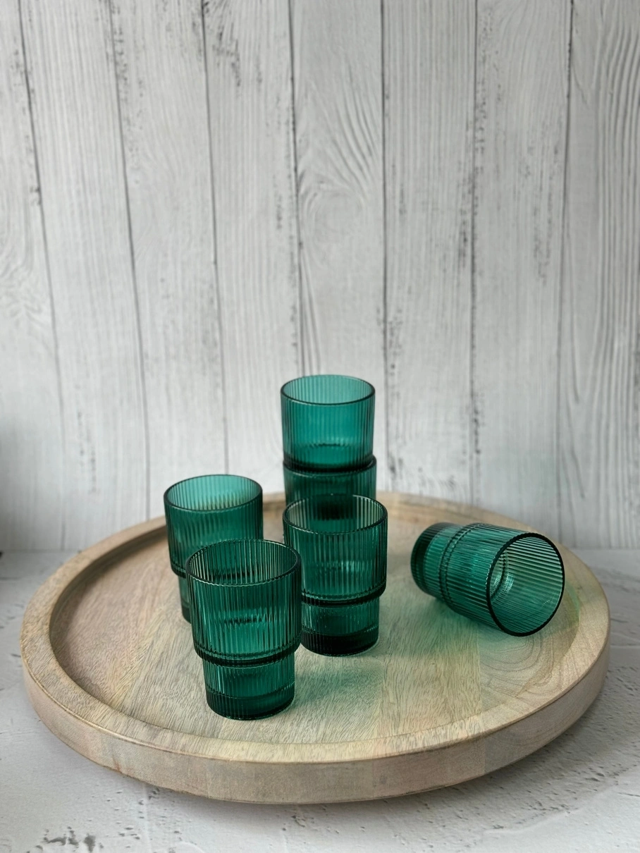 Green glasses on a round wooden tray against a white wooden background.