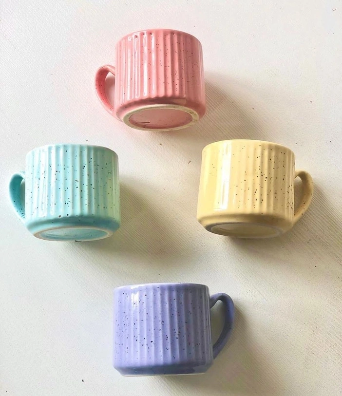 Four pastel-colored mugs with speckled designs on a light background.