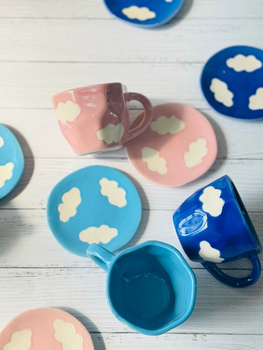 Colorful mugs and plates with cloud designs on a wooden surface.