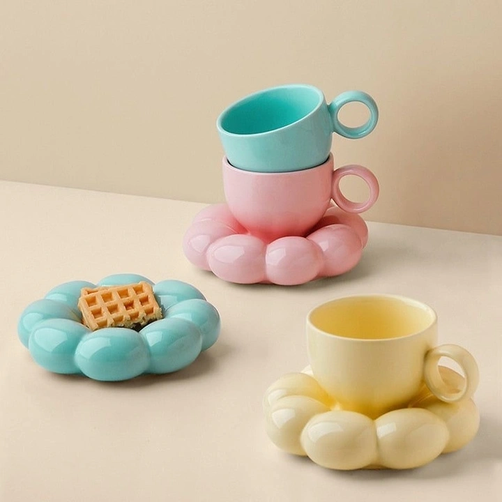 Three pastel-colored cups on matching cloud-shaped saucers, one with a small waffle.