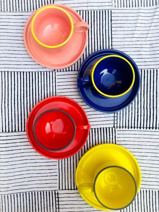 Four colorful cups with saucers on a striped fabric.