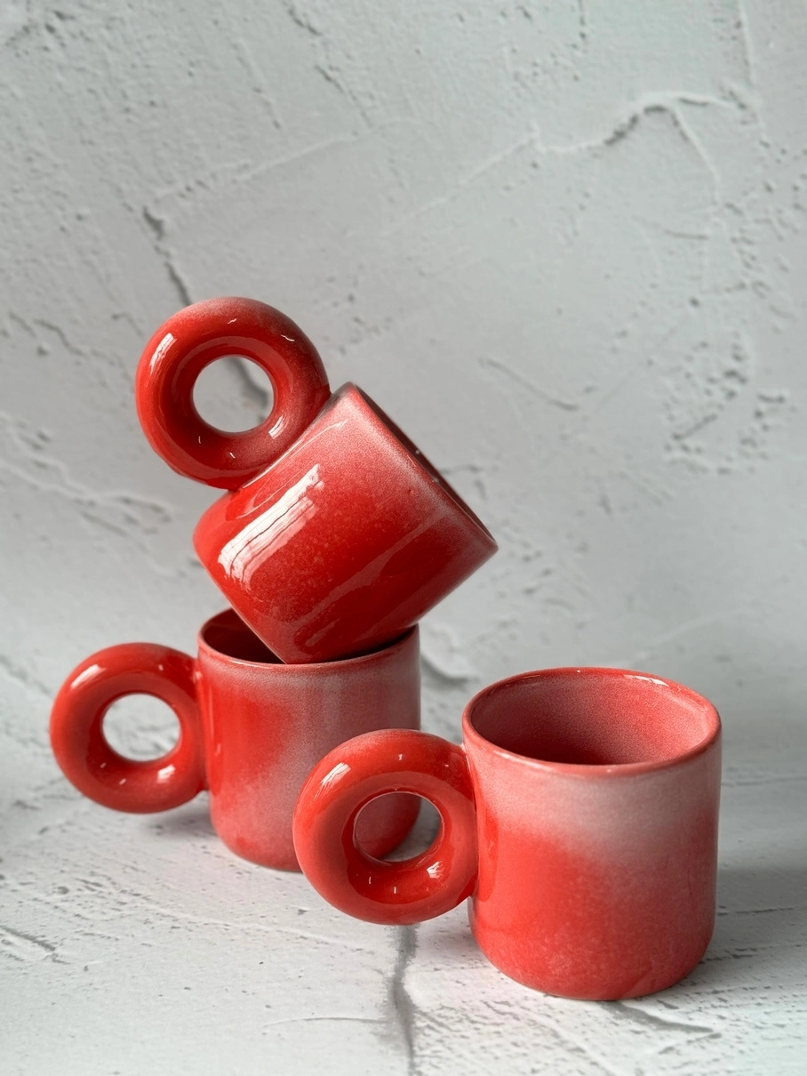 Four red ceramic mugs stacked asymmetrically against a textured white background.