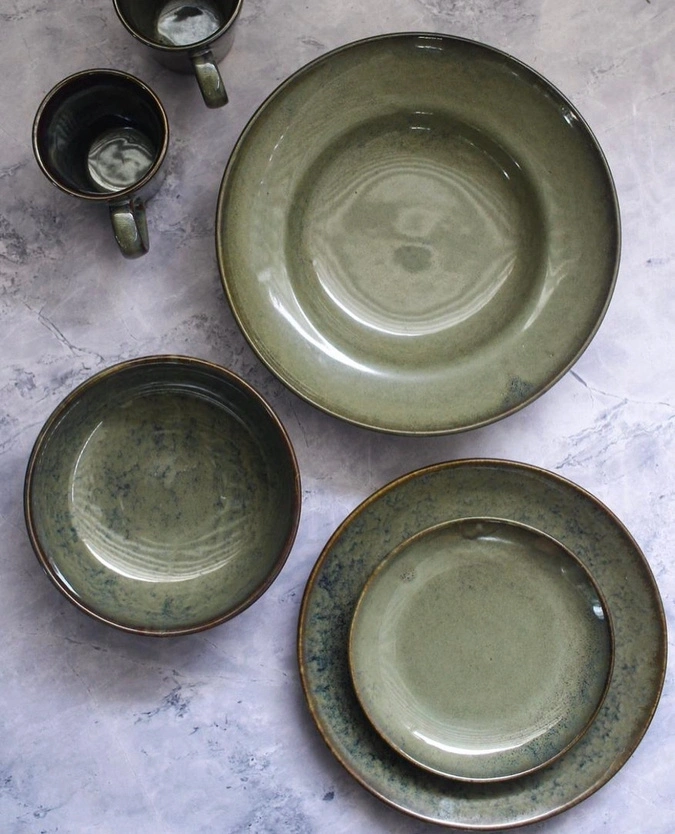 A set of green ceramic dishes and cups on a marble background.