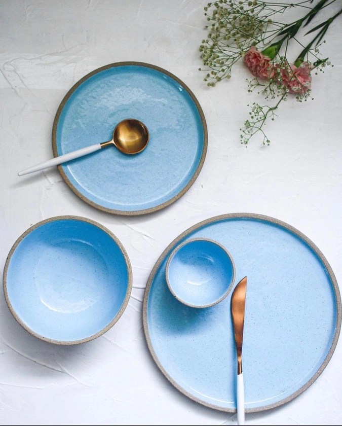 A set of blue ceramic dishes and gold-colored cutlery on a white surface with flowers.