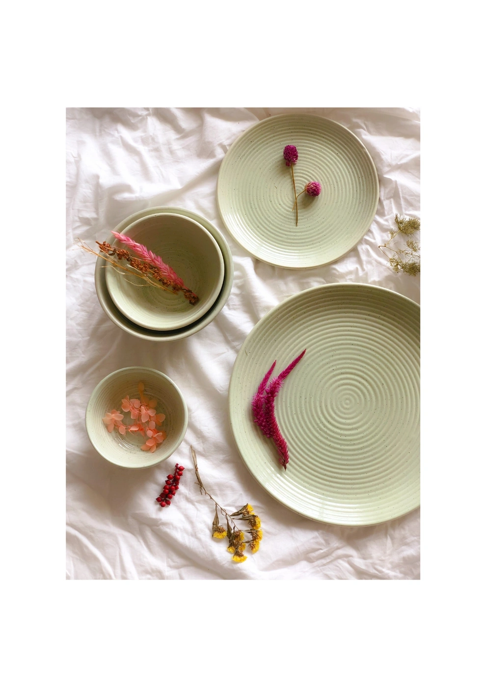 Ceramic dishes with dried flowers on a crinkled white cloth.