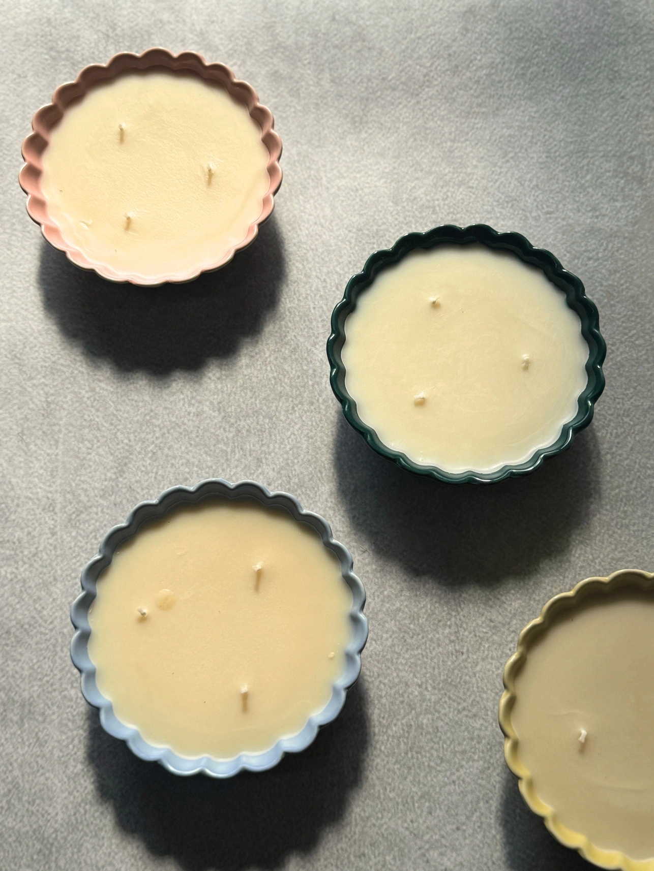 Four scalloped-edge candles in sunlight casting shadows.