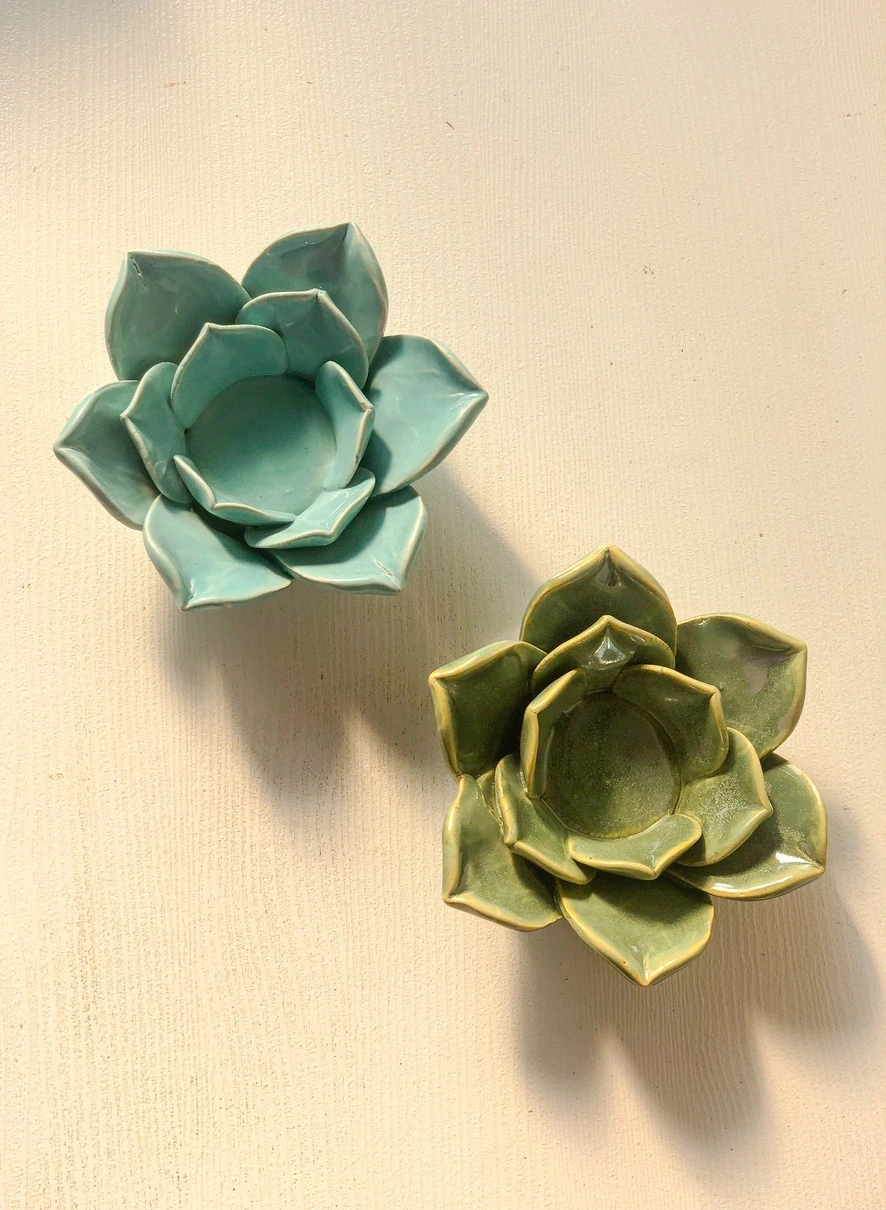 Two ceramic lotus flower bowls, one teal and one green, on a textured surface.