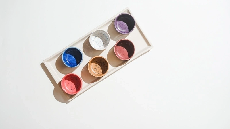 Seven colorful ceramic bowls on a tray against a white background.