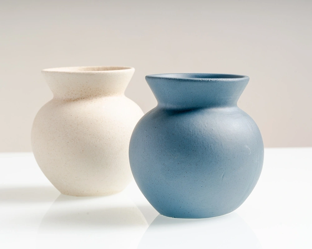 Two ceramic vases, one beige and one blue, on a white surface.