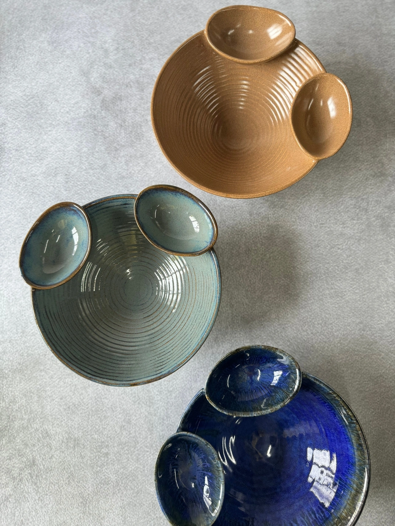 Three nested ceramic bowls in brown, green, and blue on a gray surface.