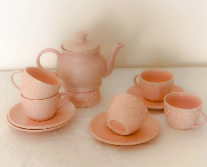 A pastel pink tea set with patterned teapot and matching cups on saucers.