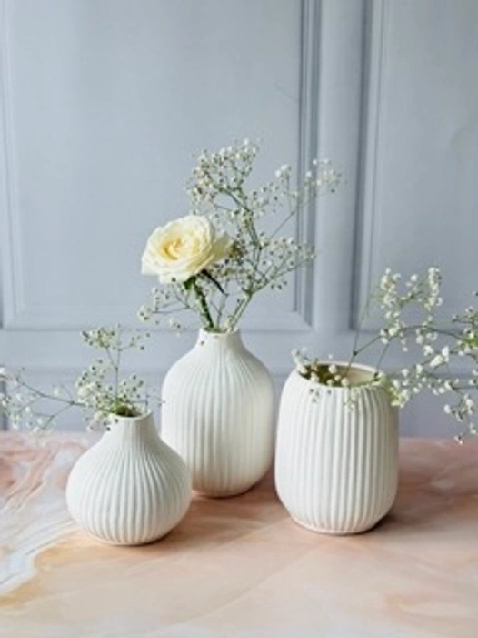 Three white ribbed vases with white flowers on a marbled surface against a grey backdrop.