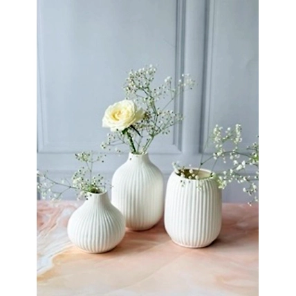 Three white ribbed vases with white flowers on a marbled surface against a grey backdrop.