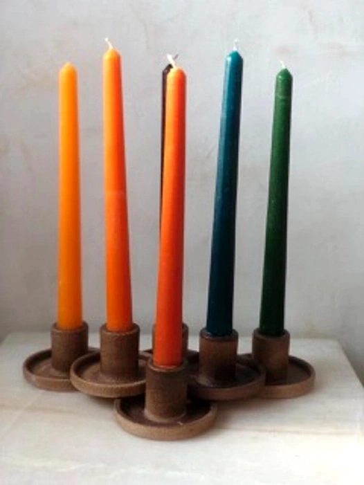 Five tall, unlit candles in orange, yellow, blue, and green, in rustic brown holders.