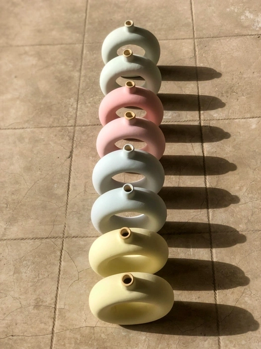 A line of colorful ceramic donut-shaped vases on a tiled floor with shadows.