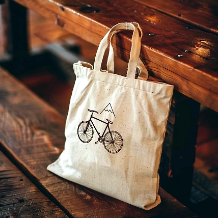 A beige tote bag with a bicycle and mountain graphic, resting on a rustic wooden table.